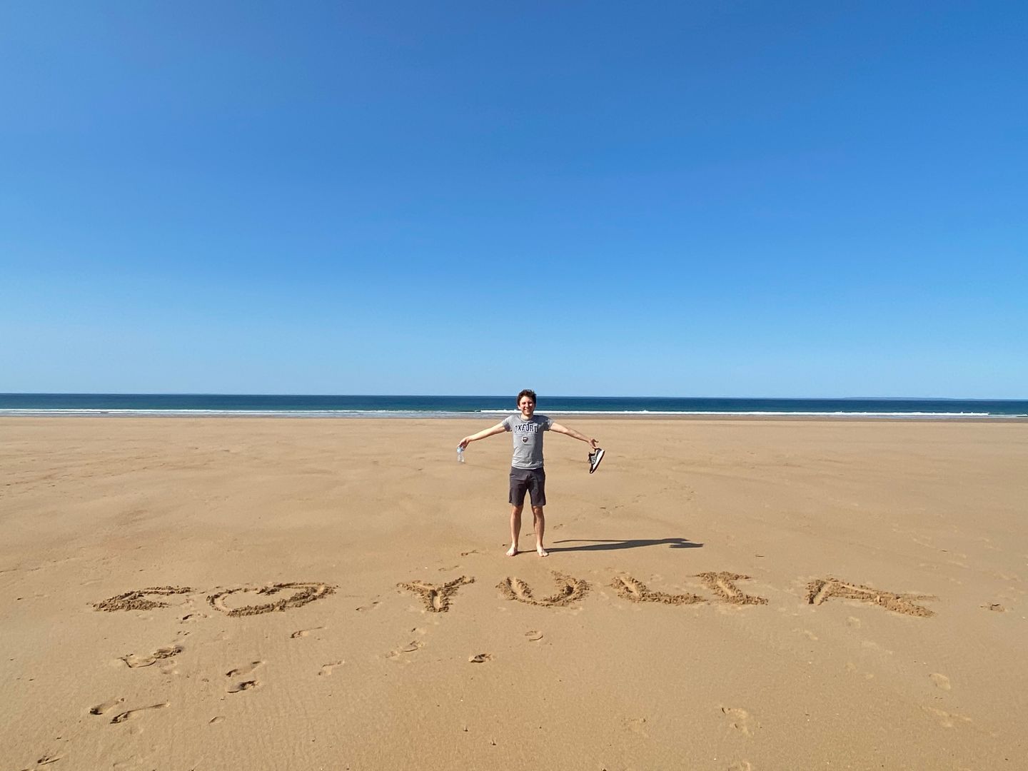 A person standing on a beach with the word go yulia written in the sand.