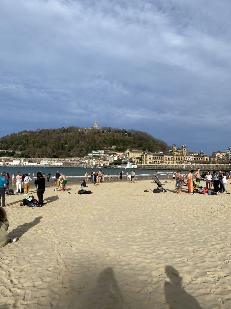 A group of people on a sandy beach with a building in the background.