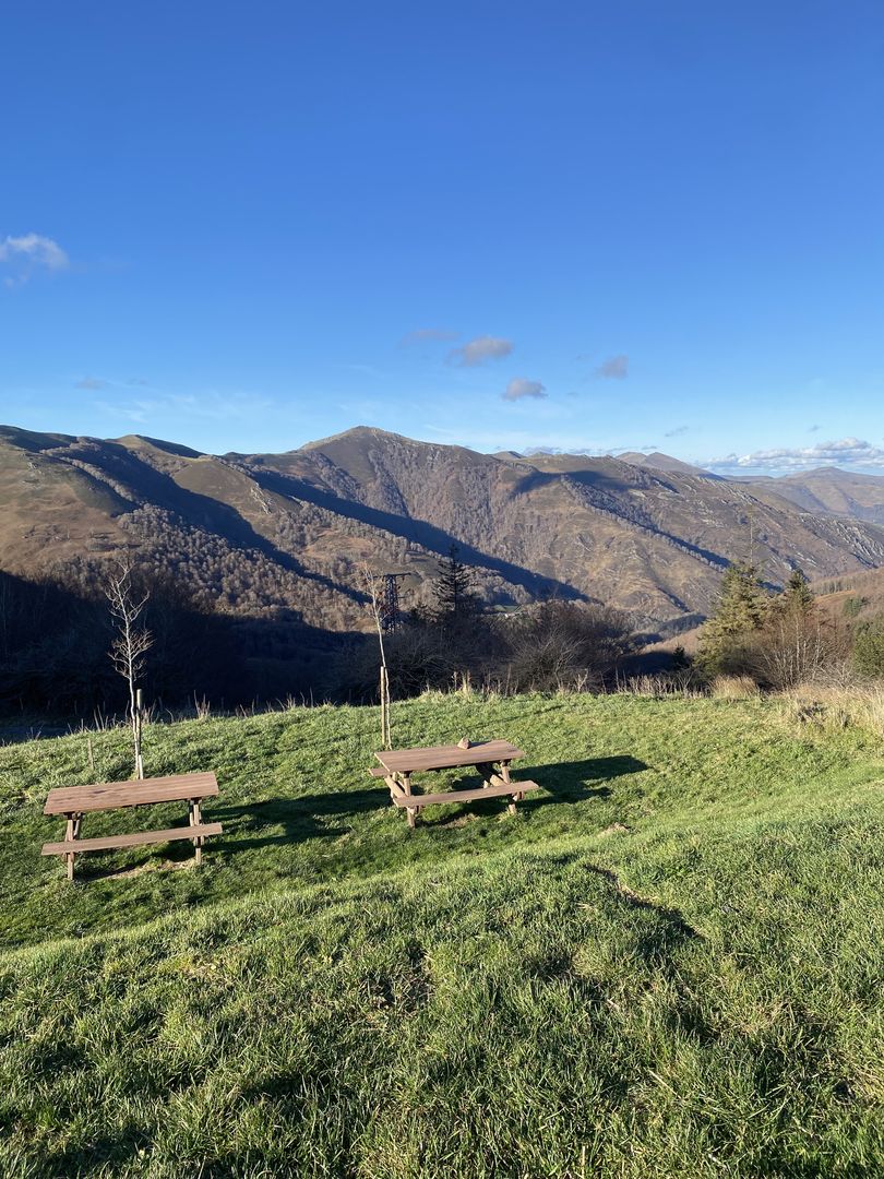 Two picnic tables on a grassy hill overlooking the mountains.