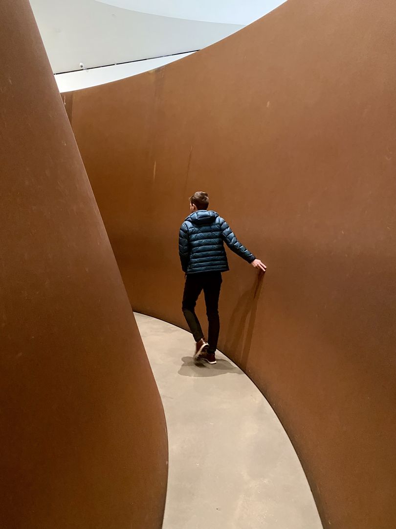 A man standing in front of a brown curved wall.