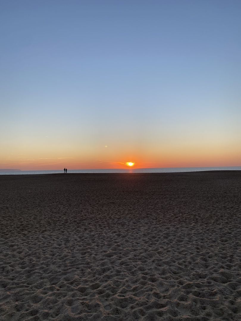 The sun is setting over a sandy beach.