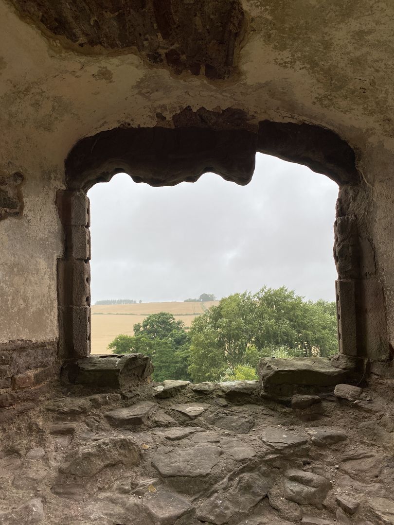 A window in an old castle with a view of a field.
