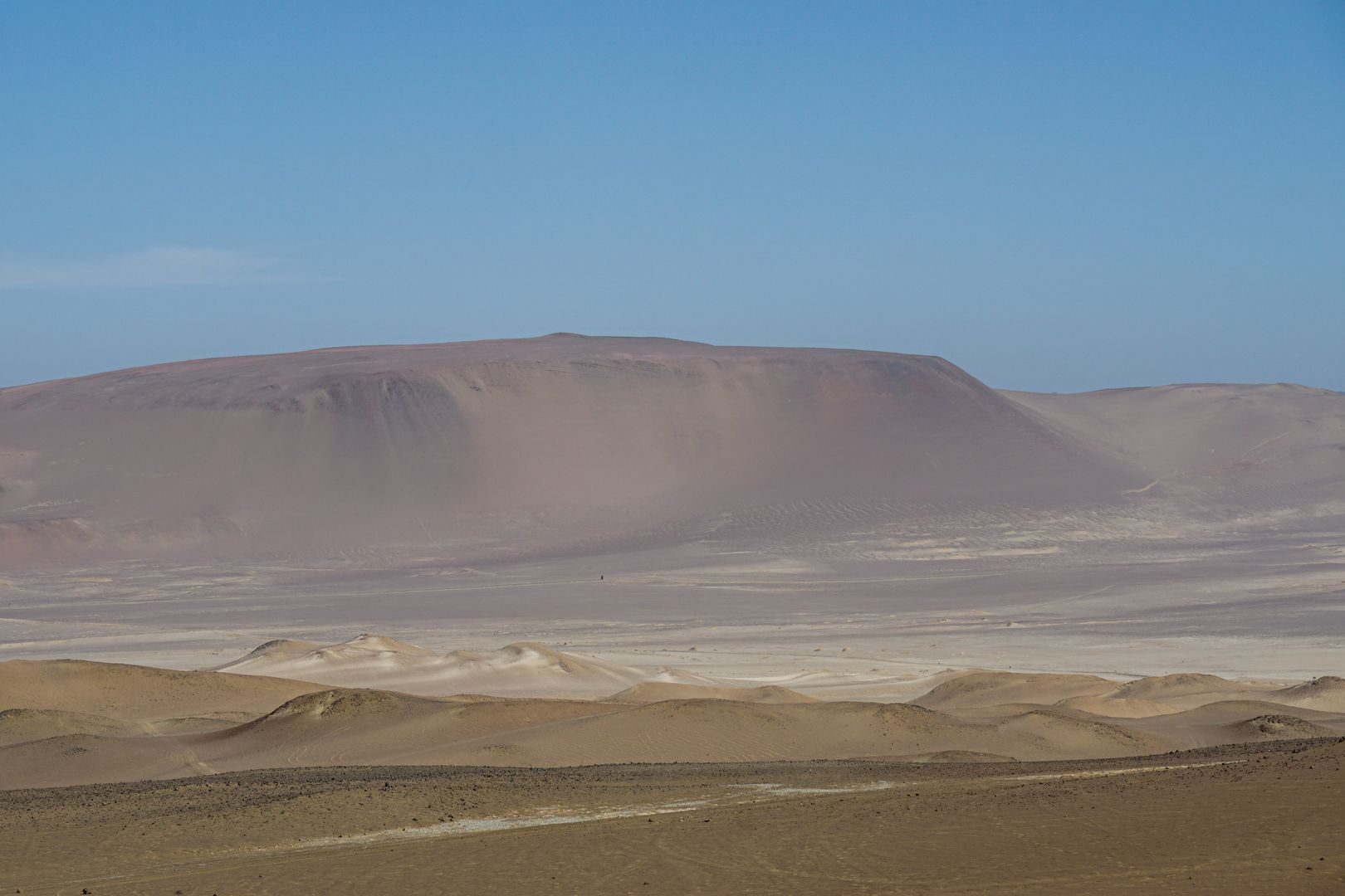 A desert landscape with sand dunes and a mountain in the background.