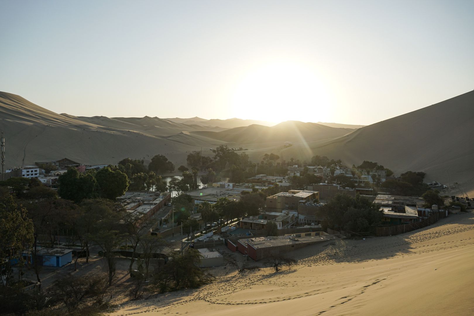 A town in the desert with sand dunes in the background.