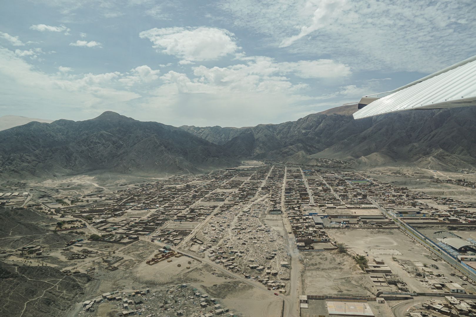 A plane flying over a city with mountains in the background.