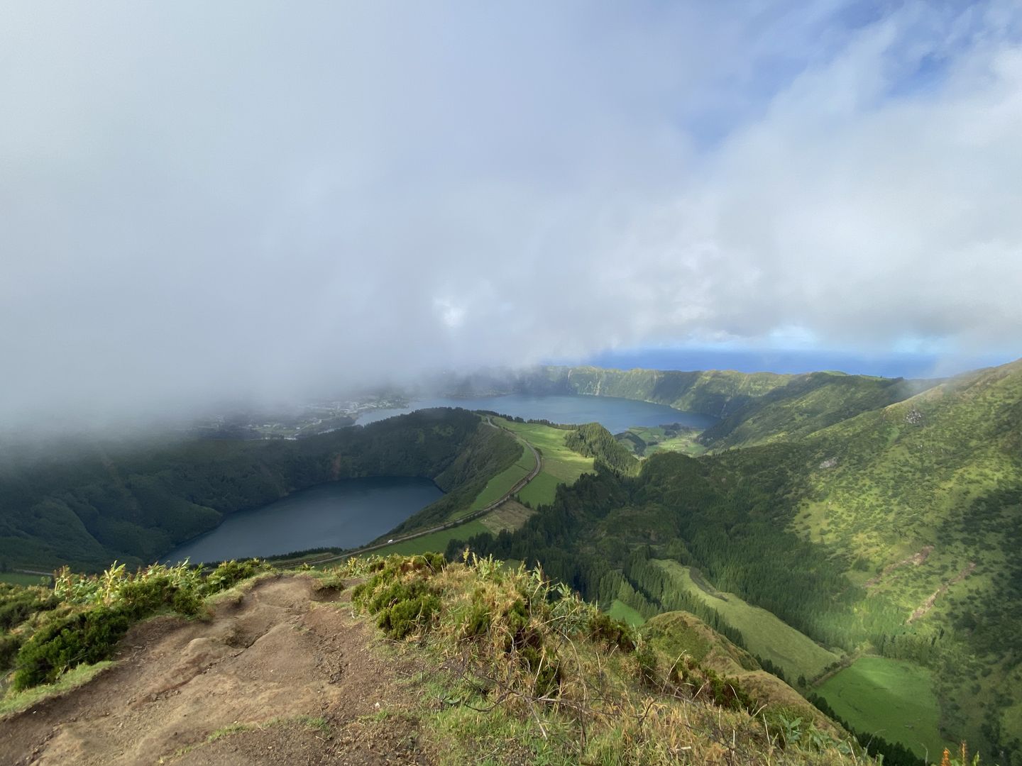 A view from the top of a mountain overlooking a lake and clouds.