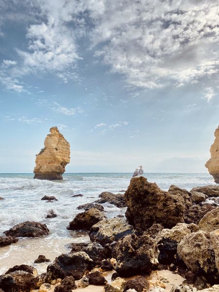 Two rock formations on the beach with a cloudy sky.